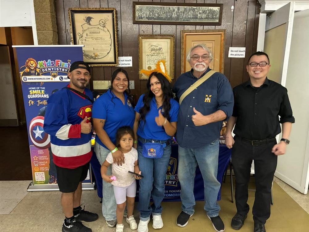 A group of adults and a child posing beside the Kids First Dentistry banner at the October show.